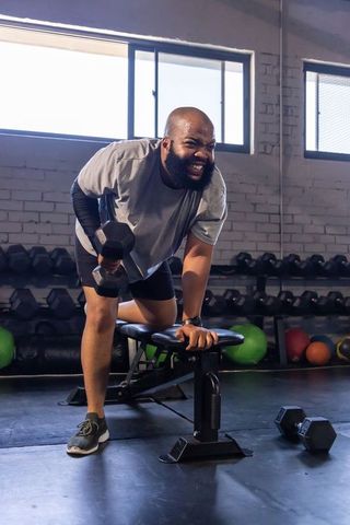 Male performing single-arm dumbbell row on bench in brick-walled gym, strength training