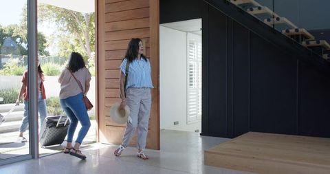 Host welcoming friends arriving at modern home through pivot door, sunlit entry moment