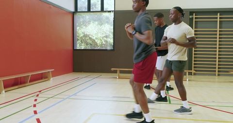 Diverse male athletes performing squat jumps on indoor gym court for team fitness training
