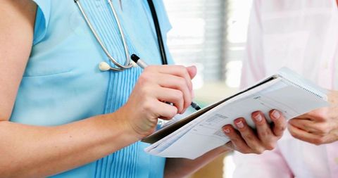 Clinician Writing Patient Notes on Clipboard During Medical Consultation, Stethoscope Visible