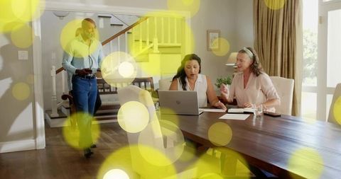 Home office collaboration reviewing documents and typing on laptop at wooden table with yellow bokeh