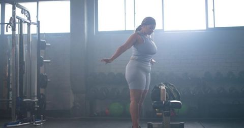Strong Female Athlete Balancing and Stretching Near Bench in Sunlit Industrial Gym