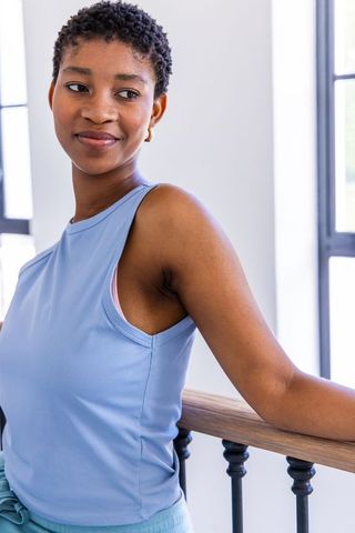 Confident woman leaning on wooden handrail by windows wearing light blue sleeveless top