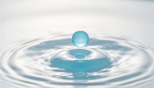 Blue droplet hovering above rippling water, creating crown splash and gradient reflection