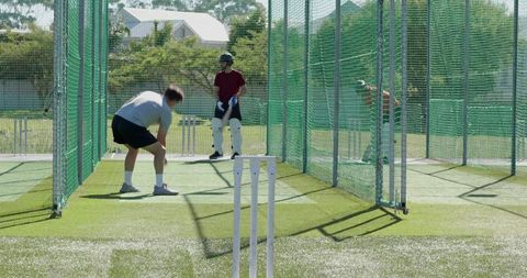 Cricket batting practice in outdoor nets with helmeted batsman and white stumps