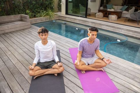 Young Men Meditating by Pool on Sunny Deck for Wellness and Mindfulness