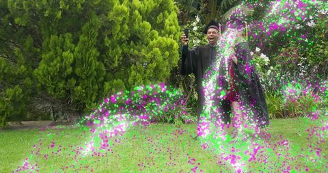 Graduates celebrating with confetti burst on lawn taking selfie in cap and gown