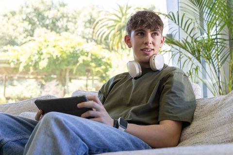 Teen relaxing on couch with tablet and headphones, home tech lifestyle in bright room