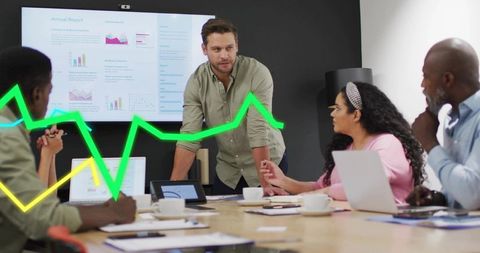 Team leader presenting analytics in boardroom with laptops, charts, green data overlays