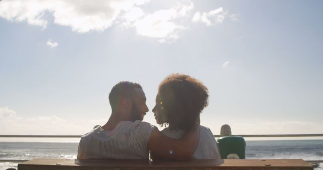 Romantic diverse couple sitting, embracing and kissing on sunny promenade, copy space. Summer, vacation, romance, love, relationship, free time and lifestyle, unaltered.