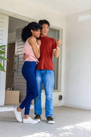 Young couple hugging at new home doorway while holding keys, celebrating move-in