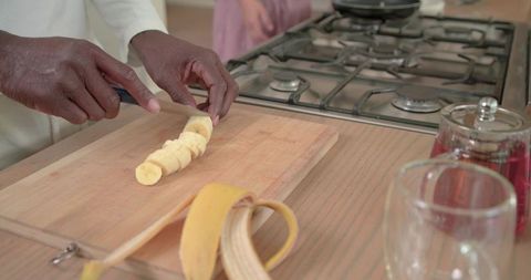 African american couple slicing banana on wooden cutting board hands at stove home kitchen