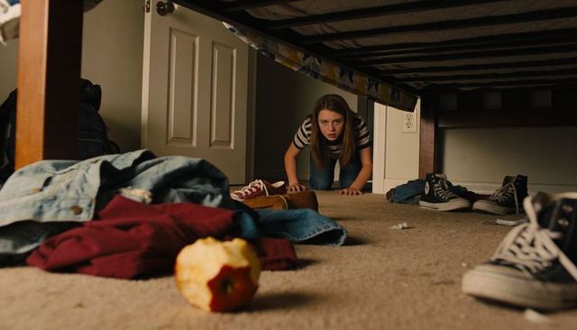 Teen crawling under bed discovering hidden corner with bitten apple in foreground