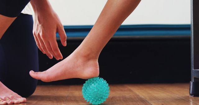 A person is using a textured massage ball to relieve tension in their foot, with copy space. Foot self-massage tools like this are commonly used for plantar fasciitis relief and to stimulate circulation.