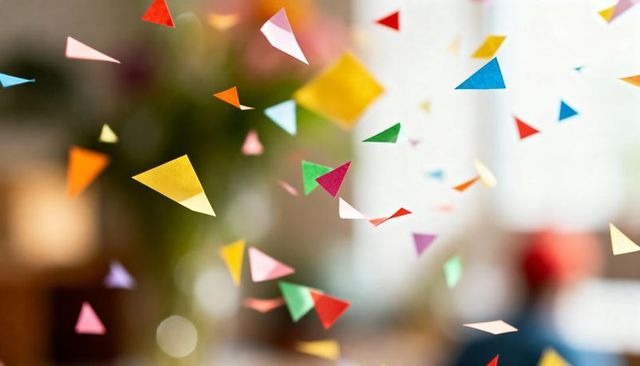 Colorful triangular paper confetti floating in soft-focus living room with flower bokeh