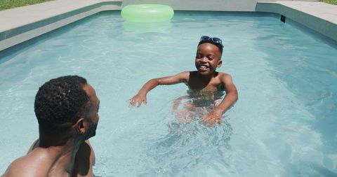 Father and son splashing in backyard pool, smiling child with sunglasses, summer playtime