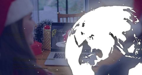 Woman in santa hat arranging laptop and gold polka-dot gift with digital globe overlay