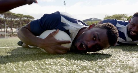 Happy rugby players scoring try on sunlit field