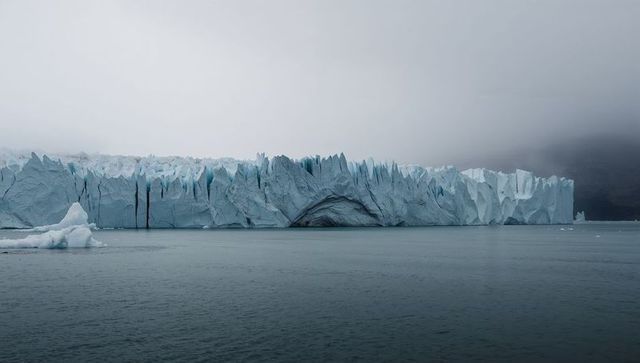 Coastal glacier face with crevasse arch, moody mist and floating ice in polar waters