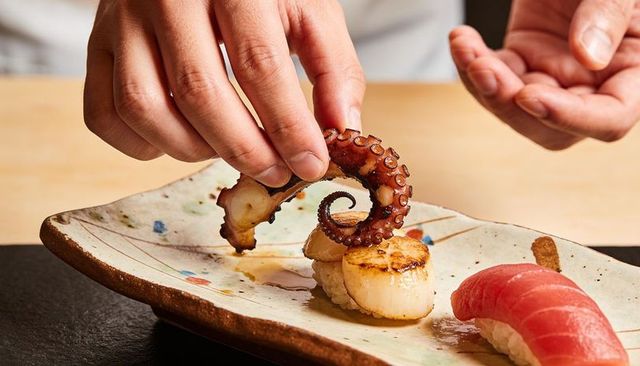 Chef placing grilled octopus on scallop and tuna nigiri for elegant sushi plating