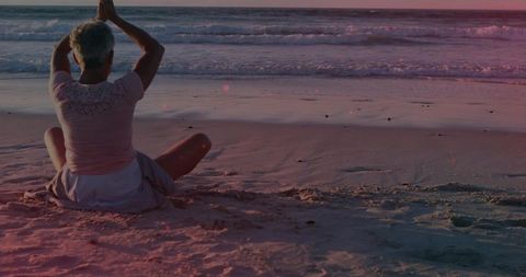 Senior woman practicing yoga on beach at golden hour, meditation and relaxation
