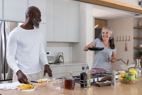 Diverse couple cooking together in modern kitchen flipping pancake and preparing fruit