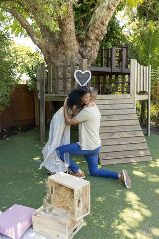 African american couple embracing during romantic backyard proposal under large tree