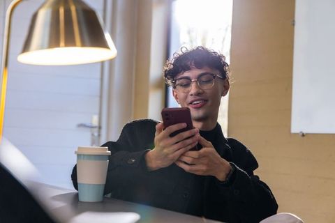 Young professional checking smartphone while relaxing in backlit coworking cafe