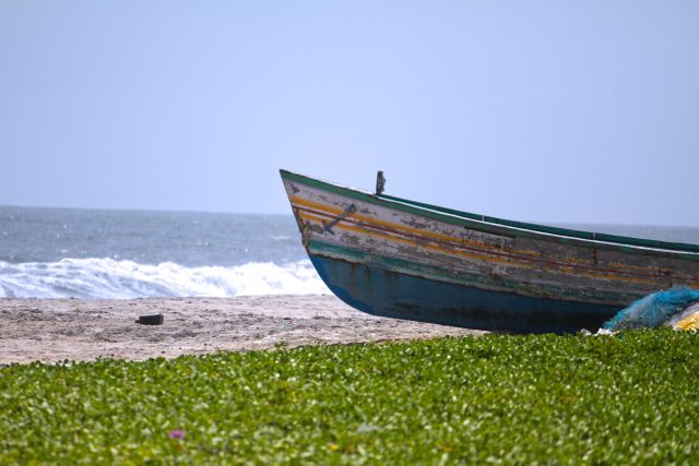 Old boat resting on sandy beach with ocean waves in background. Rustic, weathered atmosphere ideal for travel, adventure, solitude, escape themes.