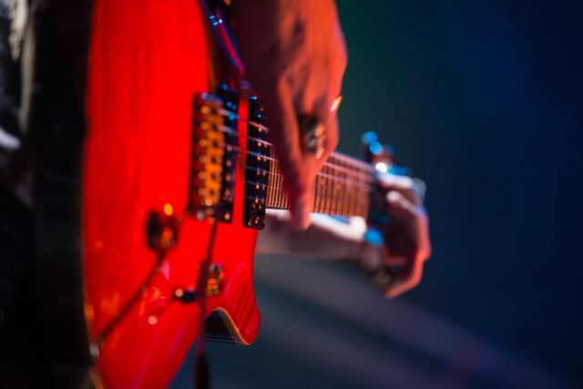 Close-up view of a guitarist playing an electric guitar on stage in a nightclub. Ideal for use in articles, blogs, and promotional materials related to live music, concerts, nightlife, and musical performances. Perfect for illustrating the energy and atmosphere of live music events.