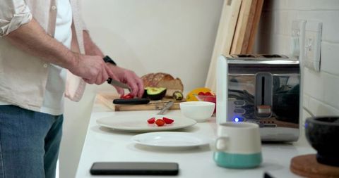 Man Slicing Vegetables in Modern Kitchen with Toaster and Smartphone