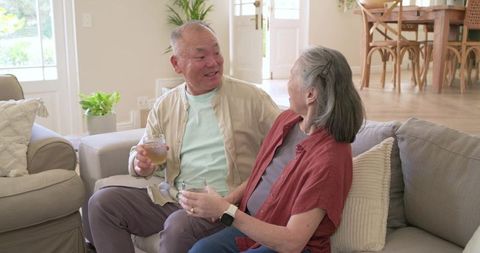 Senior couple sharing drinks and tapping smartwatch while relaxing on sofa