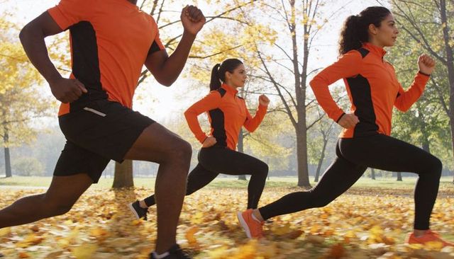 Three athletes lunging in autumn park wearing orange and black training tops