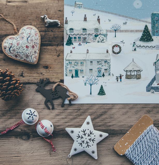 Festive Christmas decorations displayed on a wooden table, featuring rustic village scene drawing, heart ornament, pine cone, reindeer, white star, and bells with snowflakes. Perfect for holiday greeting cards, winter-themed prints, Christmas craft ideas, and seasonal blog posts.
