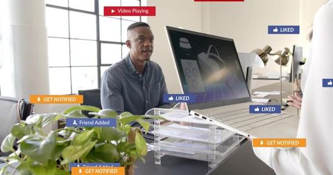 Talking black man showing laptop to colleague in modern office with social media icons
