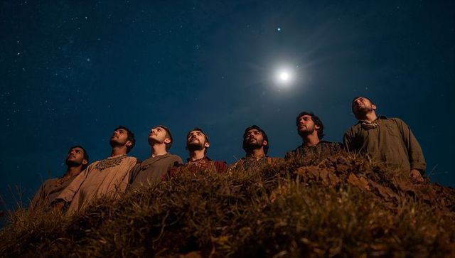 Seven men gazing at moonlit night sky from grassy ridge under full moon