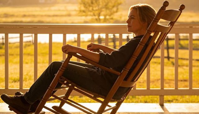 Woman relaxing in rocking chair on porch at golden hour overlooking pasture and river view