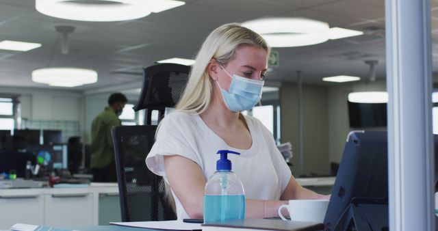 Caucasian woman in face mask using tablet in office. Office, work, communication, health, covonavirus, hygiene, architecture, unaltered.