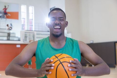 African american basketball player shouting while holding ball on indoor court with lens flare
