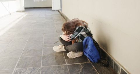 Child hugging knees in corridor with backpack