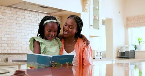 Happy Mother and Daughter Bonding Over Storybook in Kitchen