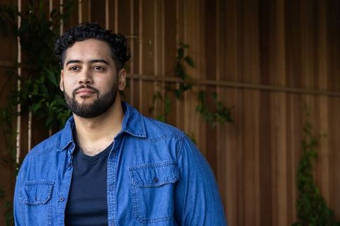 Young man standing on patio wearing denim shirt over black tee, contemplative portrait