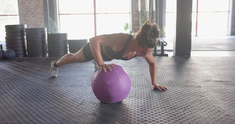 Woman Performing One-Arm Push-Up on Purple Medicine Ball in Industrial Gym