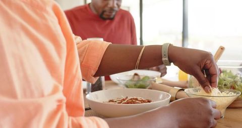 African american men preparing pasta and serving shredded cheese at kitchen table