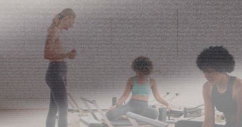 Pilates instructor guiding women on reformers in studio while timing workout and balancing