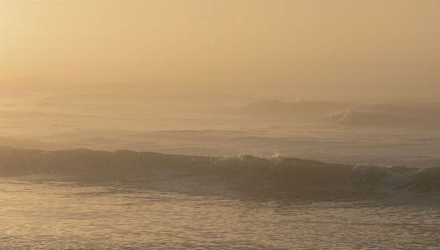 Glowing golden ocean at sunrise with rolling waves reflecting light and misty horizon