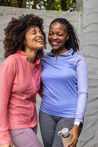 African american women laughing on patio in activewear holding water bottle and smartwatch