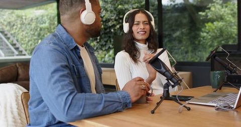 Diverse cohosts recording podcast in bright home studio with microphones and laptop