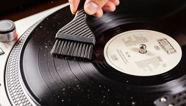 Cleaning vintage vinyl record with carbon fiber brush on turntable, closeup dust removal