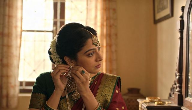 Adjusting indian bride wearing maroon saree and gold jewelry at vintage dressing table